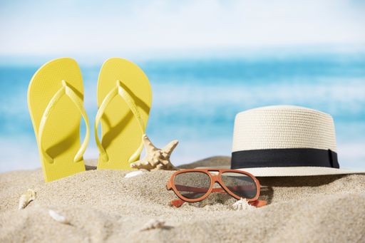 A hat, slippers, sunglasses and a starfish on the sand on the ocean background