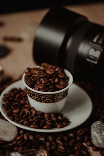A vertical shot of a coffee cup with roasted beans on blurred background