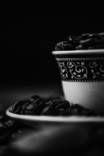 A grayscale shot of a coffee cup with roasted beans on blurred background
