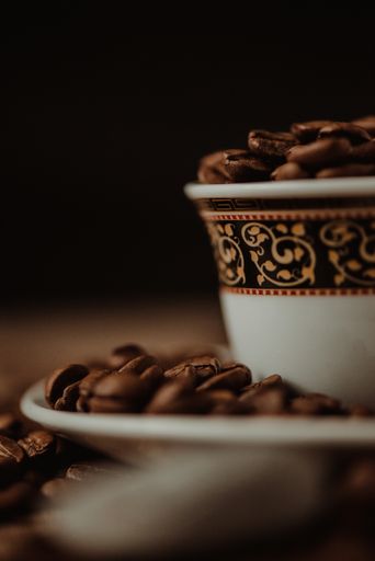 A vertical shot of a coffee cup with roasted beans on blurred background