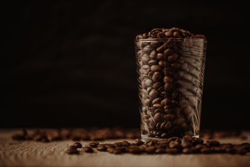 Aromatic coffee beans in transparent glass on black background