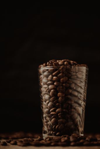Aromatic coffee beans in transparent glass on black background