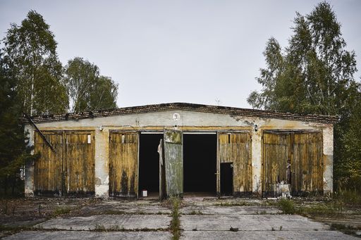 An old abandoned warehouse with broken doors surrounded by trees