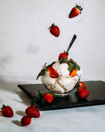 A vertical shot vanilla ice cream decorated with red strawberries falling from above