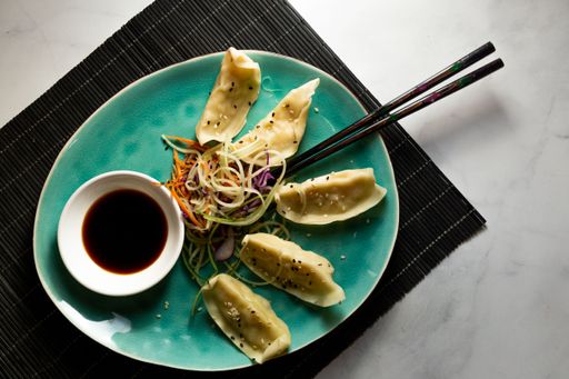 A top view of Asian dumplings served with vegetables and soy sauce on a blue plate