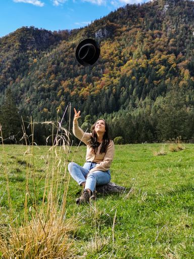 A vertical shot of a Caucasian female throwing her hat in nature