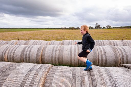 A blonde child running on a long row of round hay bales on overcast day - childhood on the farm