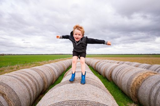 A blonde child jumping on a long row of round hay bales on overcast day - childhood on the farm