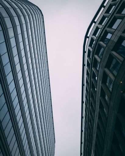 An upward vertical shot of modern tall business buildings with a white sky