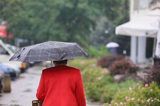 A shallow focus shot of an old female holding an umbrella while walking on a rainy weather
