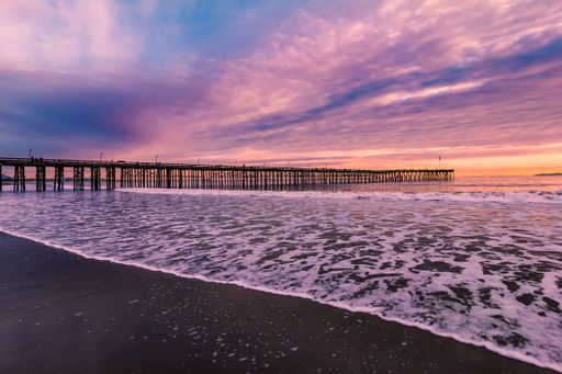 Dramatic purple sky over long pier and foamy waves at sunset, Ventura beach, California, USA
