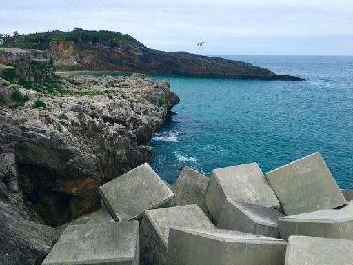 A view of a breakwater formed by concrete cubes on a scenic coastline of mountains