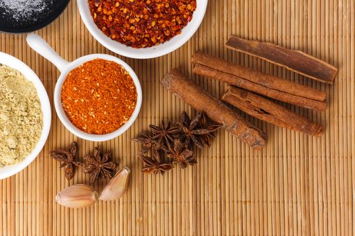A top view of cinnamon sticks, star anise, garlic, ground red chili pepper, and other condiments on a wooden surface