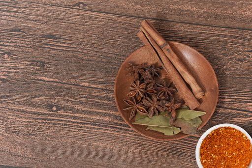 A bow of star anise, bay leaves, cinnamon sticks, as well as ground red chili pepper on the wooden table