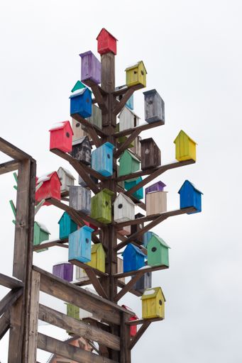 A vertical shot of different colored birdhouses next to a wooden fence