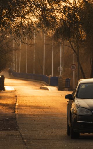 A vertical shot of a quiet street and a car driving down it in the evening