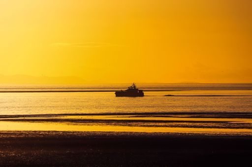 A beautiful view of a ship in the middle of a sea during orange sunset