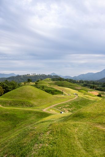 A vertical shot of bright green hills with a path under a blue sky in Gyeongsangnam-do, South Korea
