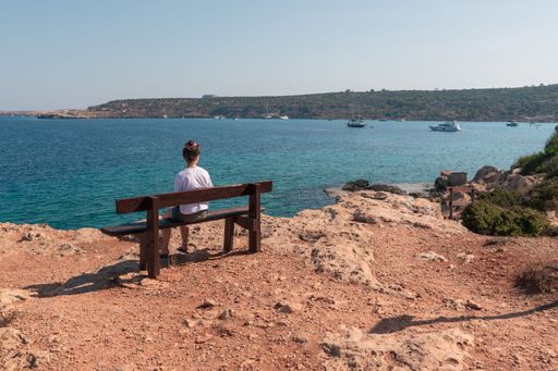 A person sitting on a bench and looking at the sea