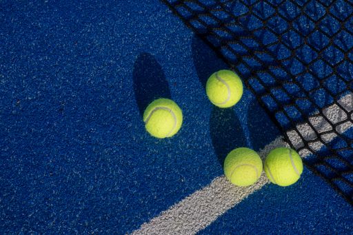 four balls near the net of a blue paddle tennis court