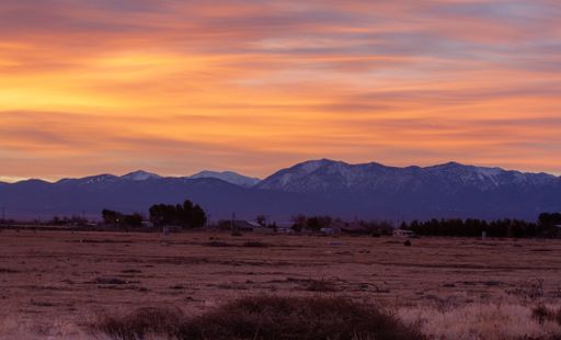 A sunset with hot warm colors over a mountainous scenery surrounding the field