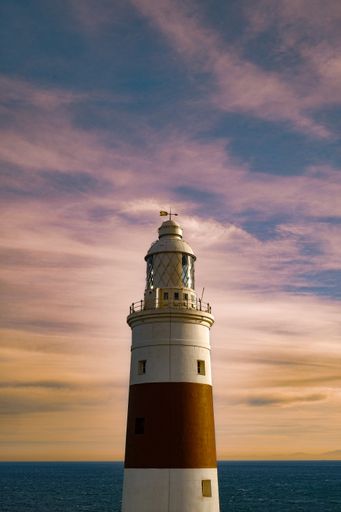 A vertical shot of a tall lighthouse with a pink cloudy sky background