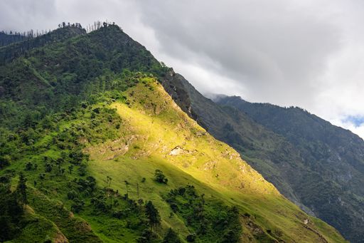 An aerial view of Nepali lower altitude mountain forests on the road from Pokhara to Jomsom near Tatopani, with green slopes and cloudy sky