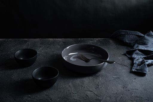 Gray ceramic bowls and plates with forks on gay surface with dark background