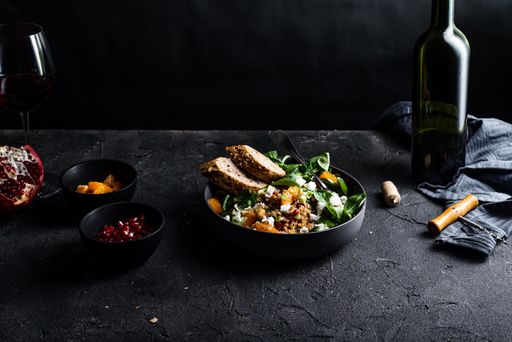 A salad with lamb's lettuce, pomegranat plate, goat cheese, mandarine and spring onion and red wine