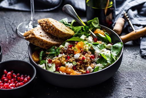 A Buckwheat salad with lamb's lettuce, pomegranat seeds, cheese, mandarine and spring onion on table
