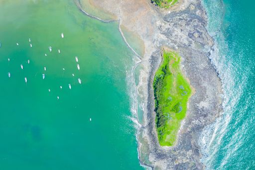 An aerial top view of boats in the ocean near a beautiful island on a summer day
