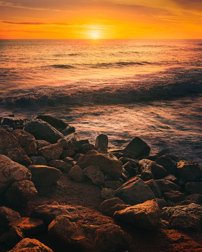 A vertical shot of a bright sunset sky over a rocky seashore