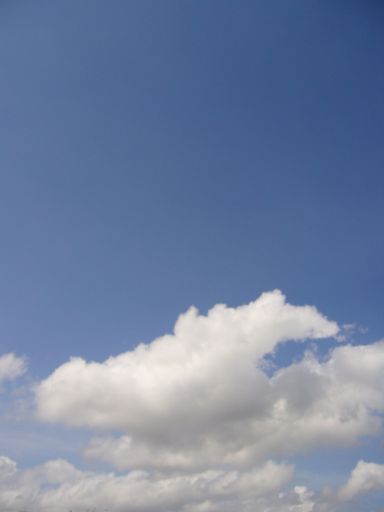 A vertical shot of a blue daytime sky with fluffy cotton-like clouds for a background