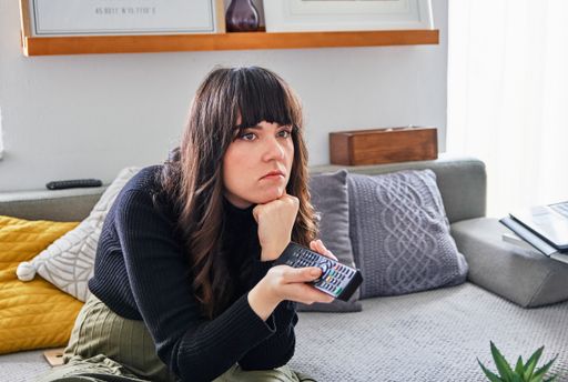 A sad Caucasian female sitting on the couch and watching  TV