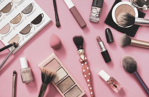 Top view of makeup accessories on pink background, overhead, directly above, flat-lay, brushes, eyeshadow, nail polish, lipstick.