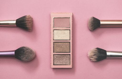 A closeup shot of an eye shadow palette with brushes on pink background