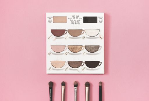 A closeup shot of an eye shadow palette with brushes on pink background