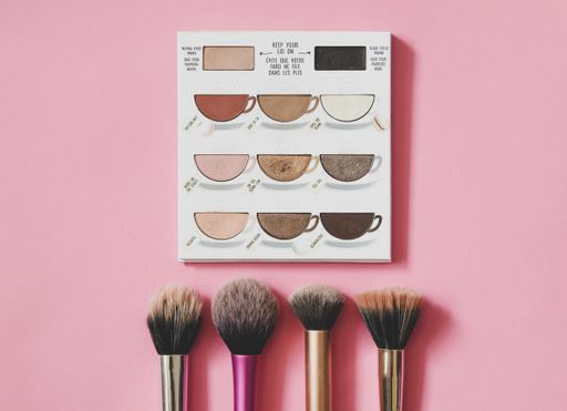A closeup shot of an eye shadow palette with brushes on pink background