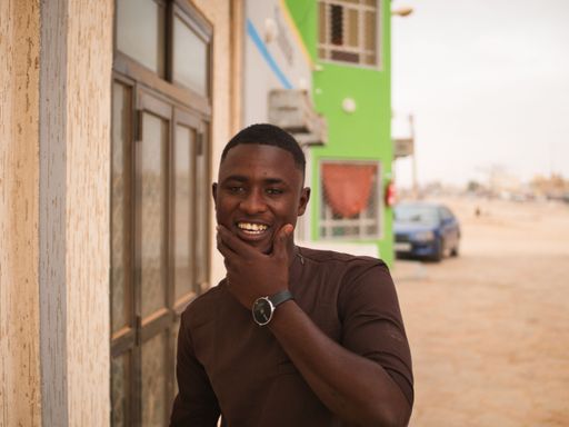 A young african man smiles to the camera with one hand on his chin