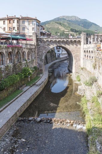 A vertical shot of a stone-made arched small bridge over a flowing Potes river in Cantabria, Spain