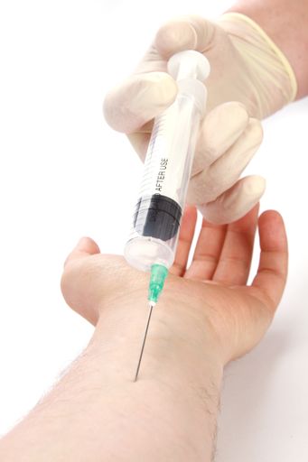 A vertical shot of a doctors hand injecting a syringe into a patients arm