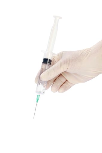 A vertical shot of a gloved doctors hand holding a syringe isolated on a white background