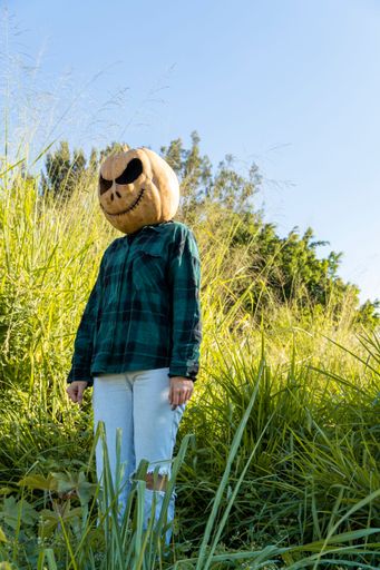 A vertical shot of a person with a carved spooky pumpkin on their head standing on a field