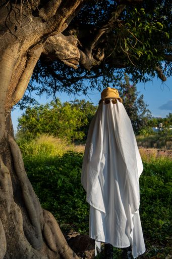 A vertical of a man dressed like a ghost for Halloween covered with a white cloth in a forest