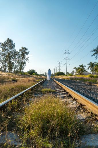 A vertical shot of a person in a funny cute ghost costume on train tracks
