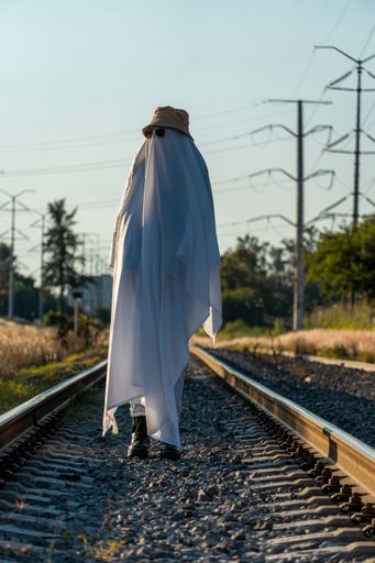 A vertical shot of a person in a funny ghost sheet costume, sunglasses, and a bucket hat on tracks