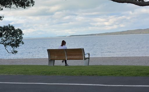 View of woman sitting on park bench at Tamaki Drive Mission Bay beach