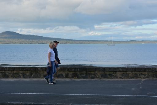 View of couple walking at Tamaki Drive Mission Bay with Rangitoto volcano island in background