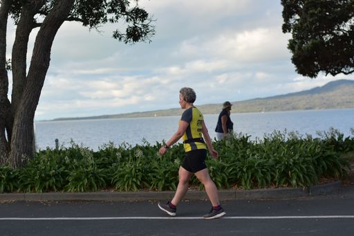 View of woman walking at Tamaki Drive Mission Bay with Rangitoto volcano island in background