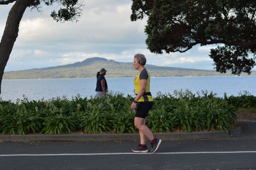 View of woman walking at Tamaki Drive Mission Bay with Rangitoto volcano island in background